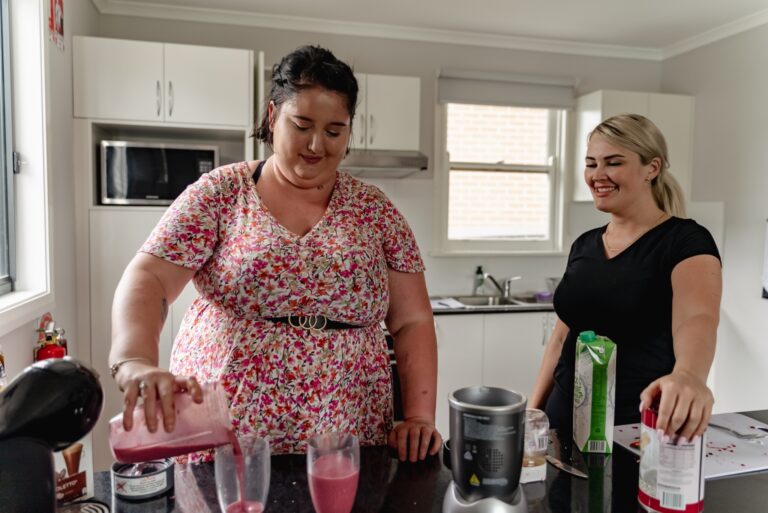 two women standing next to each other in a kitchen.