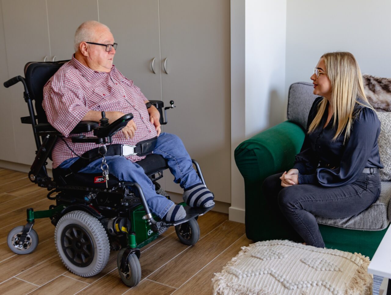 a man in a wheelchair talking to a woman in a living room.