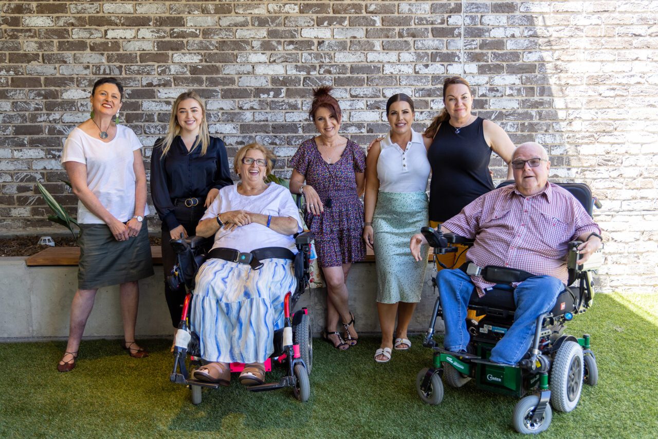 a group of people in wheelchairs posing in front of a brick wall.