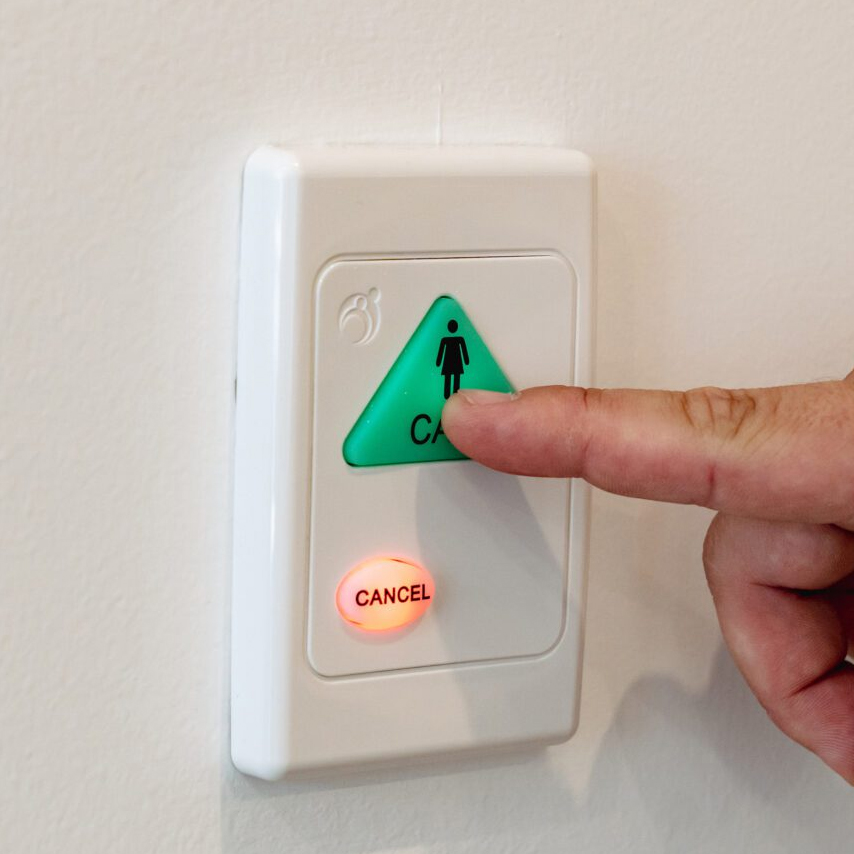 a person pressing a green call button on a wall for support with a cancel button nearby