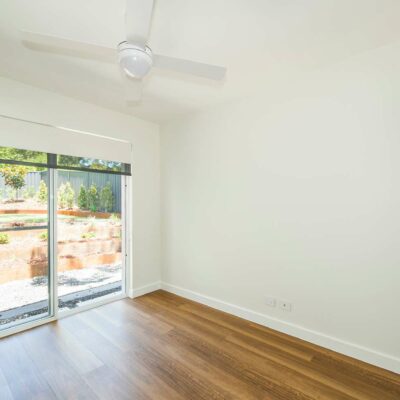 bedroom with ceiling fan, white wallls floorboards and sliding door to courtyard